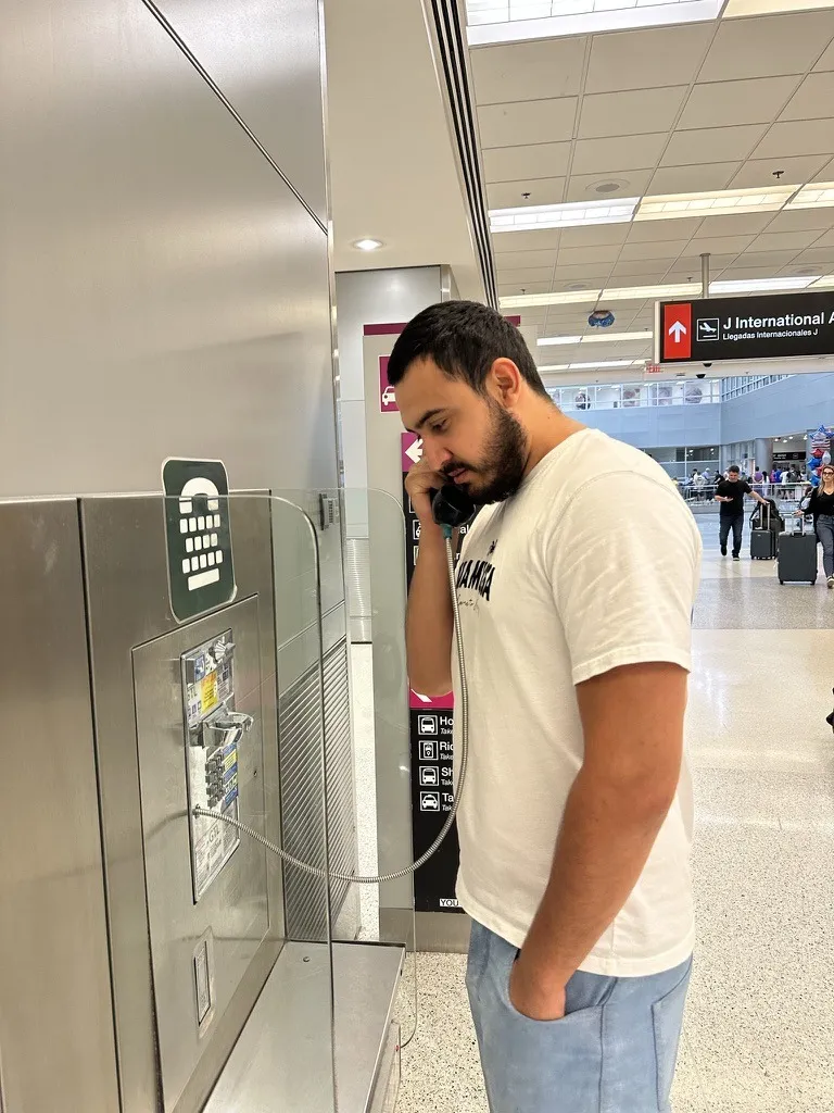 Rustam Akhadov at an airport payphone, the receiver to his ear, looking down at the keypad.